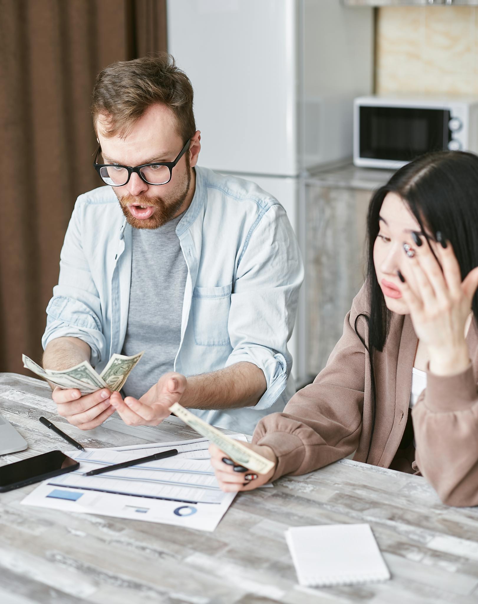 A couple is overwhelmed while handling their finances at home, counting money with stress.