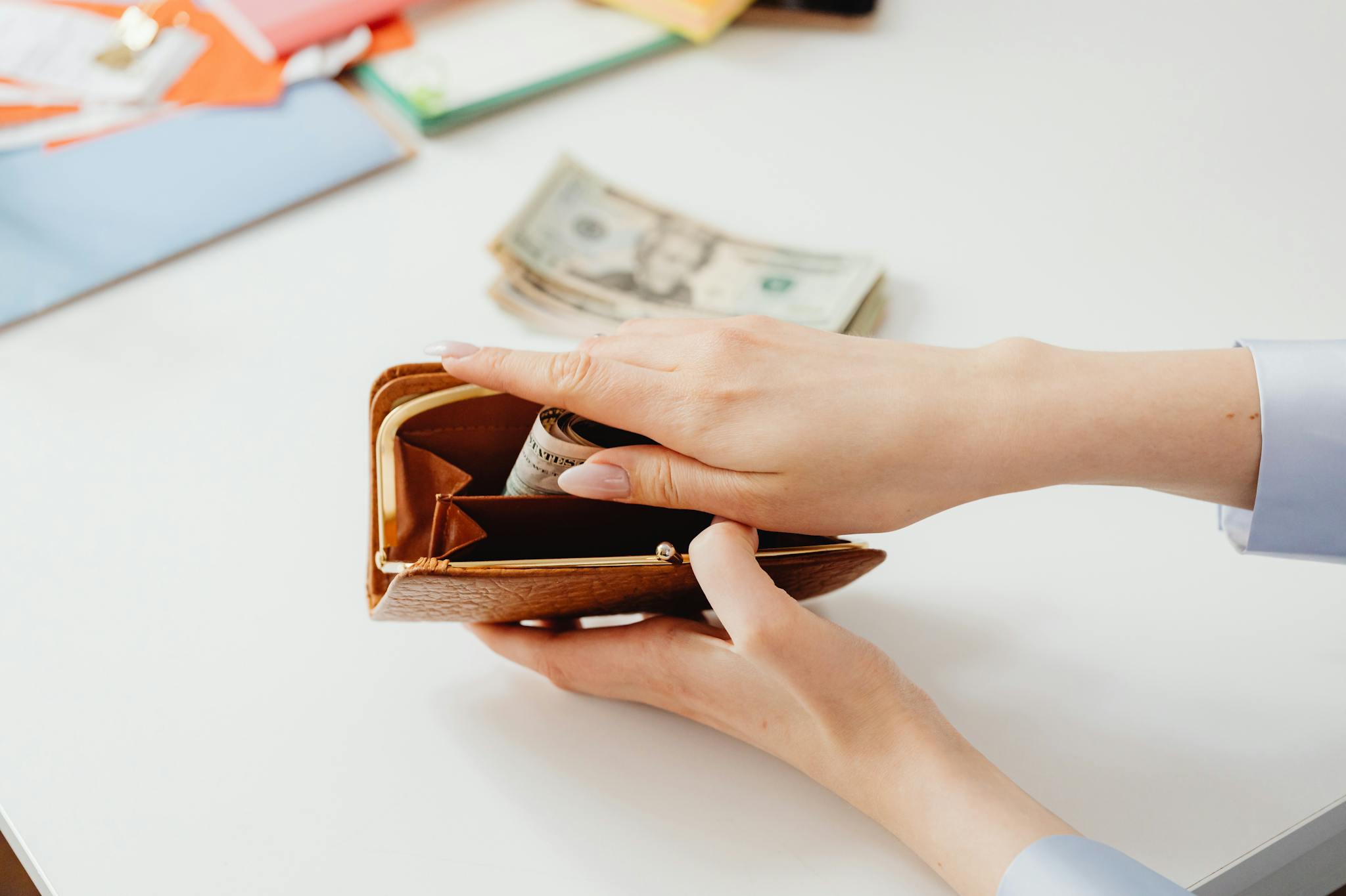 Close-up of hands placing cash into a leather wallet with bills on table.